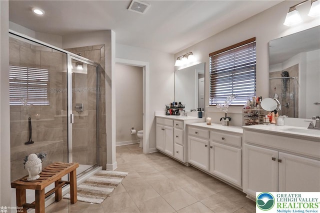 bathroom with visible vents, double vanity, toilet, a sink, and a stall shower