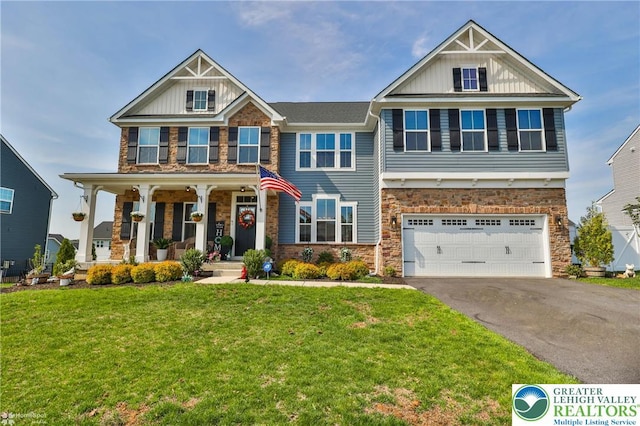 craftsman-style home featuring a garage, aphalt driveway, a front yard, stone siding, and a porch