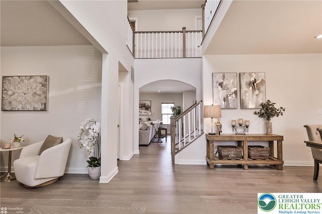 foyer entrance with arched walkways, stairs, baseboards, wood finished floors, and a towering ceiling