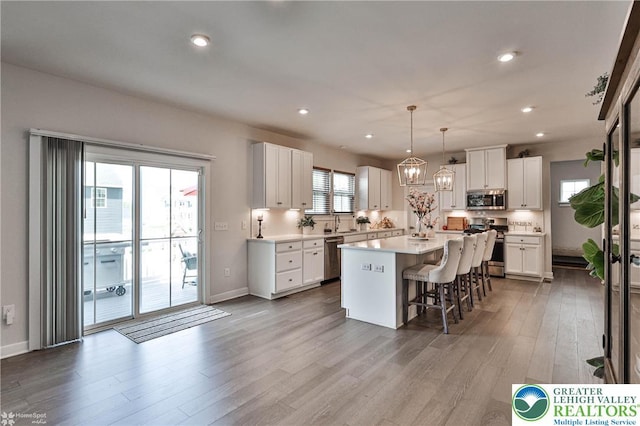 kitchen with wood finished floors, a kitchen island, a kitchen breakfast bar, white cabinetry, and appliances with stainless steel finishes