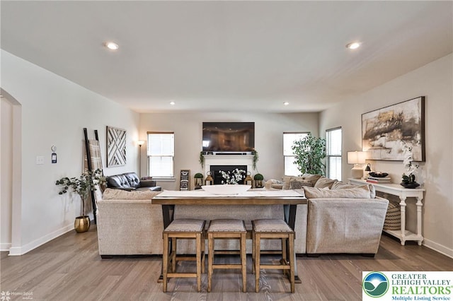 living area featuring a fireplace, arched walkways, recessed lighting, baseboards, and wood finished floors