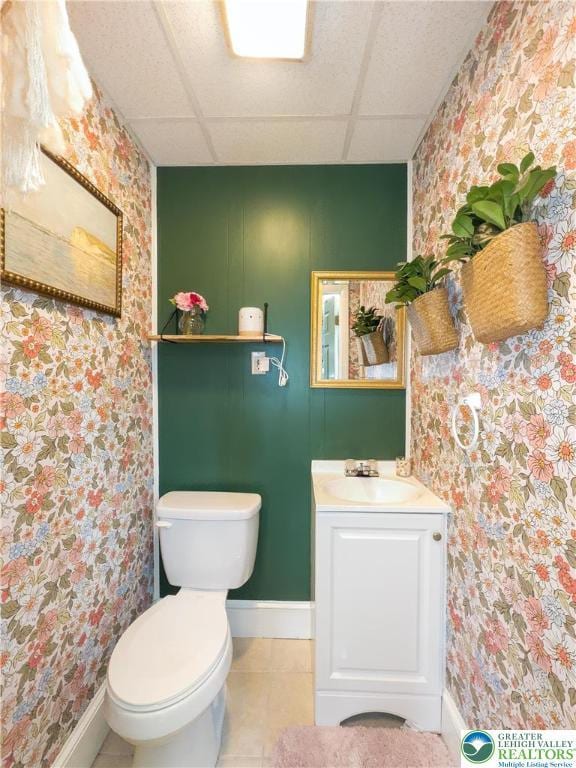 bathroom with tile patterned flooring, toilet, baseboards, wallpapered walls, and a paneled ceiling