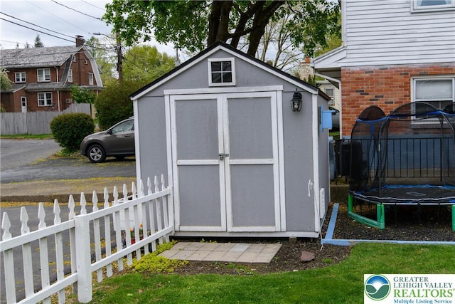 view of shed with fence and a trampoline