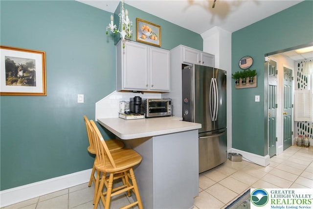 kitchen featuring freestanding refrigerator, a toaster, a breakfast bar, baseboards, and light tile patterned floors