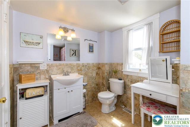 bathroom with tile patterned flooring, vanity, wainscoting, toilet, and tile walls