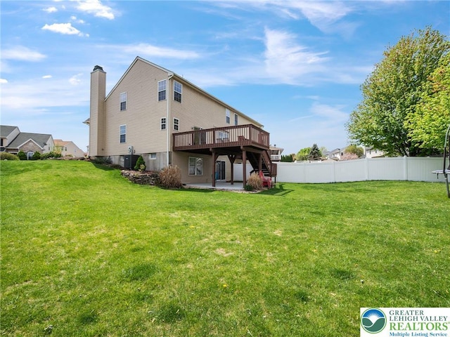 rear view of house with fence, a wooden deck, a yard, and a patio
