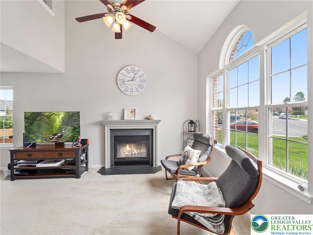 living area with carpet floors, high vaulted ceiling, a ceiling fan, baseboards, and a fireplace with flush hearth