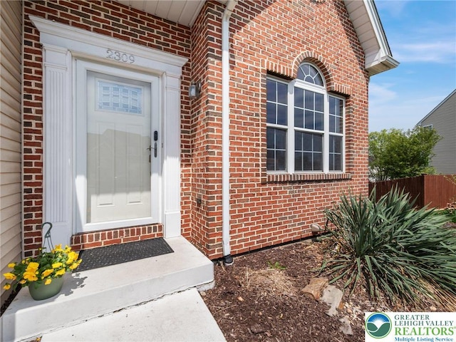 view of exterior entry featuring brick siding and fence
