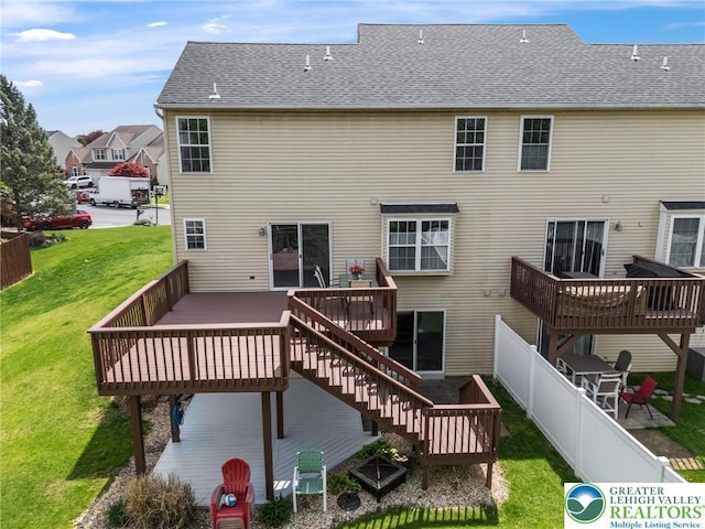 rear view of house with fence, roof with shingles, stairs, a deck, and a lawn