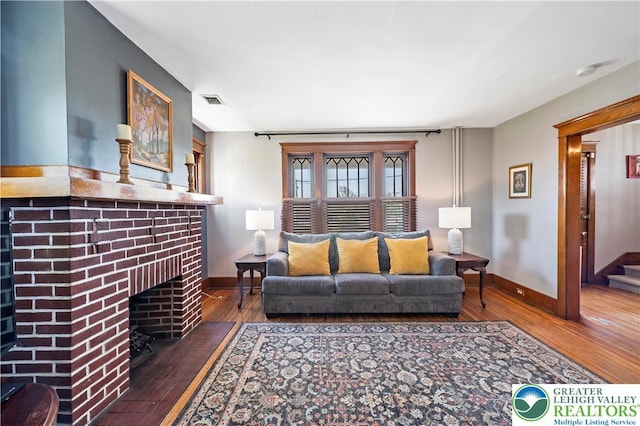 living area featuring baseboards, visible vents, hardwood / wood-style flooring, and a fireplace