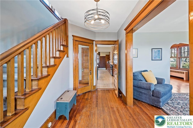 foyer with an inviting chandelier, arched walkways, radiator, stairs, and hardwood / wood-style flooring