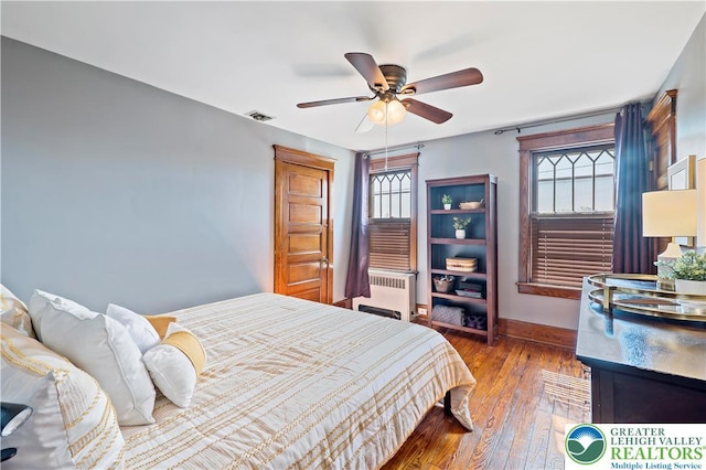 bedroom featuring ceiling fan, visible vents, baseboards, wood-type flooring, and radiator