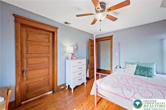 bedroom with a ceiling fan, baseboards, visible vents, and wood finished floors