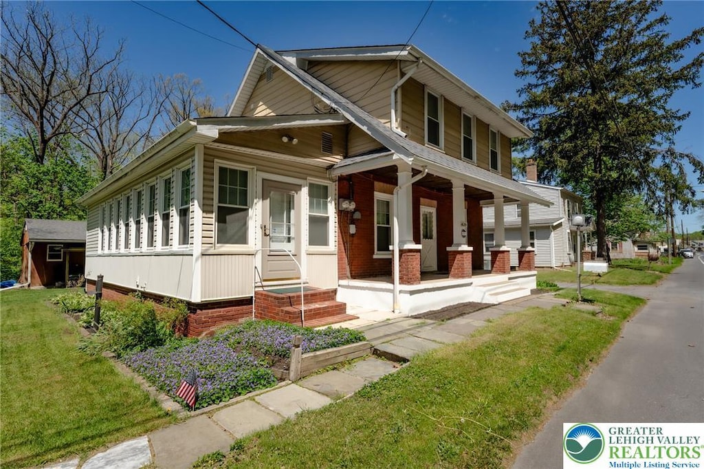 view of front facade with a porch, a front yard, an outbuilding, brick siding, and a shed