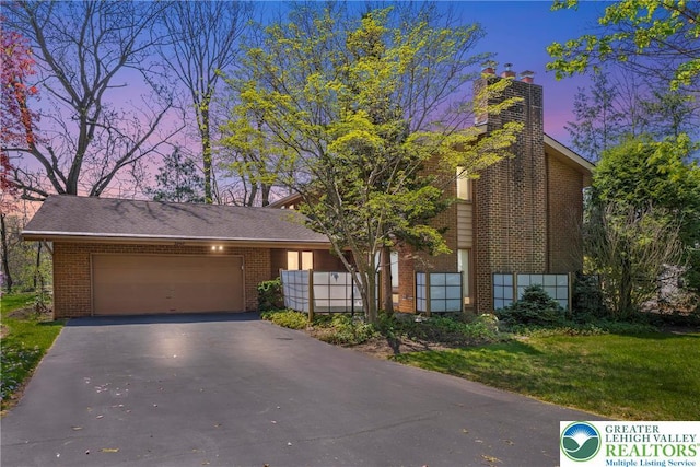 view of front of home with a front yard, a chimney, brick siding, an attached garage, and driveway