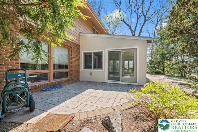 rear view of property with brick siding, a patio area, and stucco siding