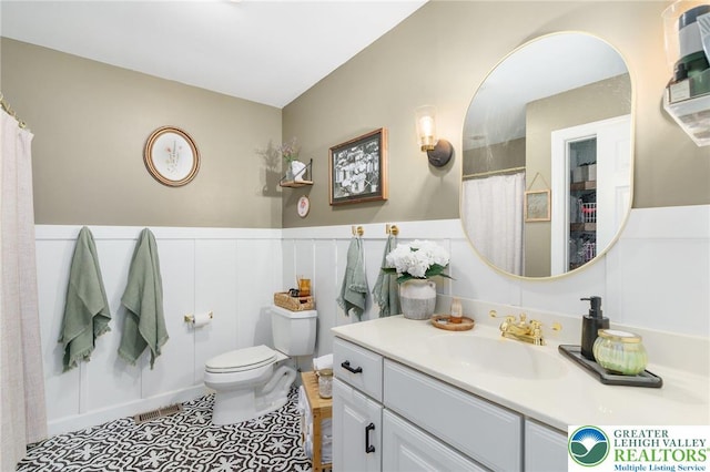 full bath with vanity, visible vents, wainscoting, a decorative wall, and toilet