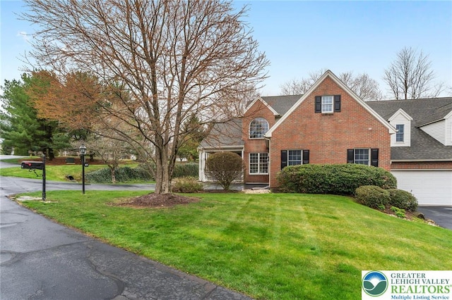 traditional-style house with a garage, a shingled roof, a front yard, and brick siding
