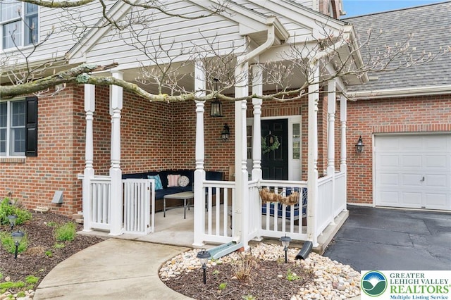 doorway to property featuring brick siding, a garage, roof with shingles, and an outdoor hangout area