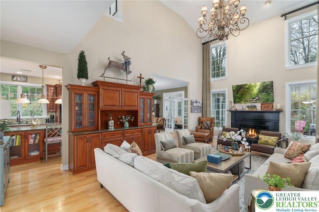 living room with light wood-style floors, high vaulted ceiling, an inviting chandelier, and a healthy amount of sunlight