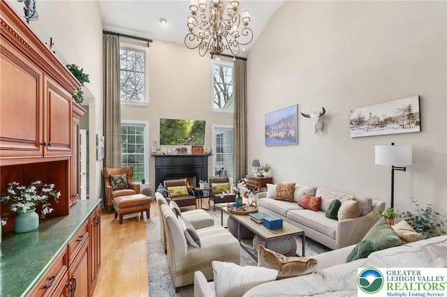living area with a lit fireplace, light wood-style flooring, a chandelier, and high vaulted ceiling