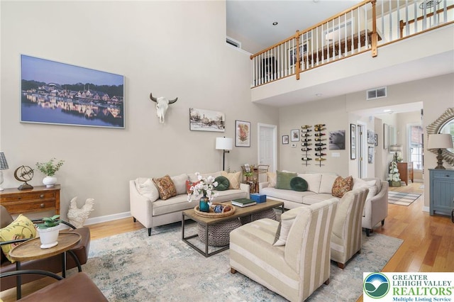 living room featuring baseboards, a high ceiling, light wood finished floors, and visible vents
