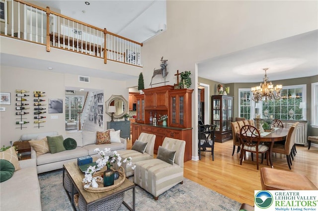 living room with a towering ceiling, visible vents, light wood finished floors, a chandelier, and stairs