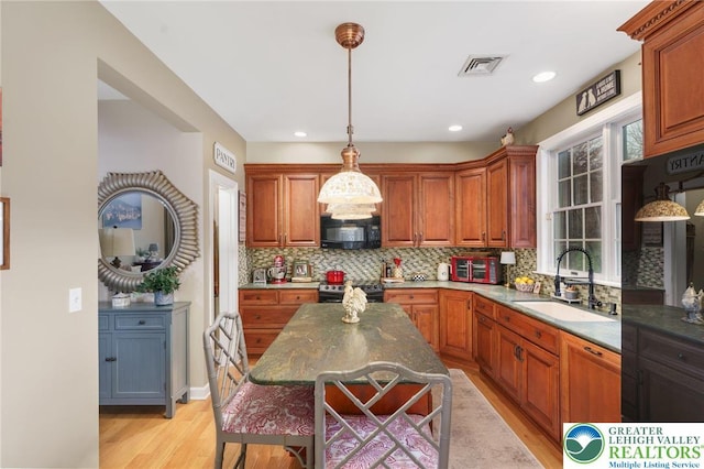 kitchen featuring a sink, a kitchen breakfast bar, light wood-style flooring, decorative backsplash, and black appliances
