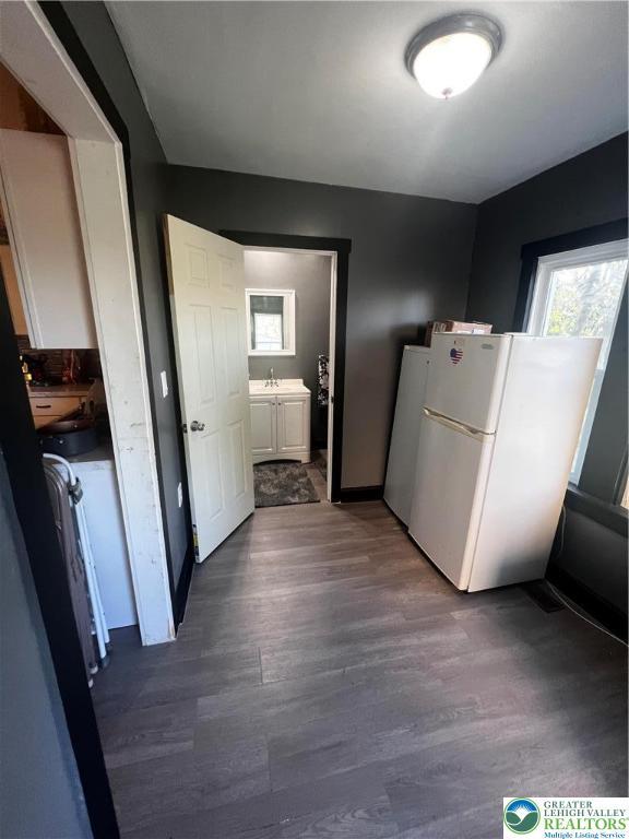 kitchen featuring freestanding refrigerator, dark wood-style flooring, baseboards, white cabinets, and a sink