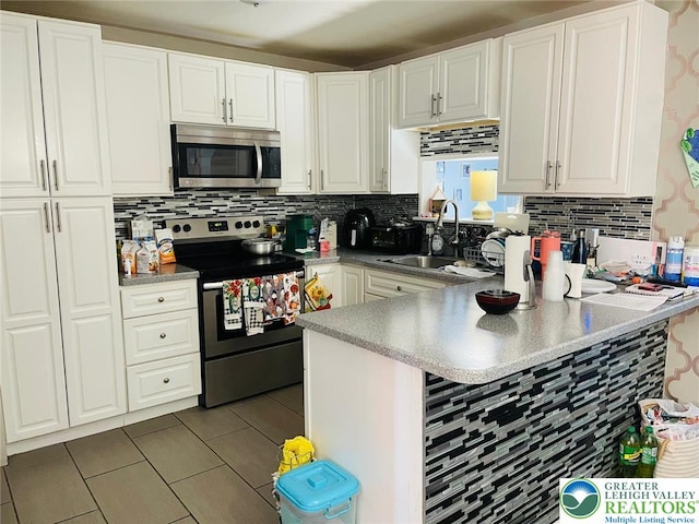 kitchen featuring appliances with stainless steel finishes, a sink, tile patterned floors, a peninsula, and tasteful backsplash