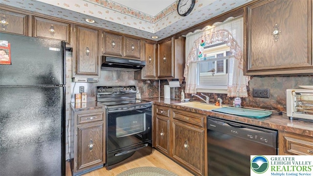kitchen featuring decorative backsplash, light wood-type flooring, under cabinet range hood, a sink, and black appliances