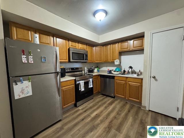 kitchen with brown cabinets, a sink, light countertops, stainless steel appliances, and wood finished floors