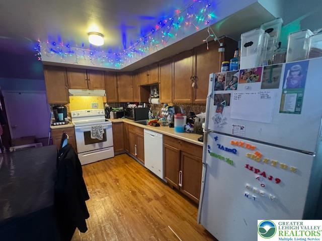kitchen featuring brown cabinets, light wood-style floors, white appliances, light countertops, and under cabinet range hood
