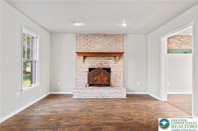 unfurnished living room with a brick fireplace, visible vents, plenty of natural light, and wood finished floors
