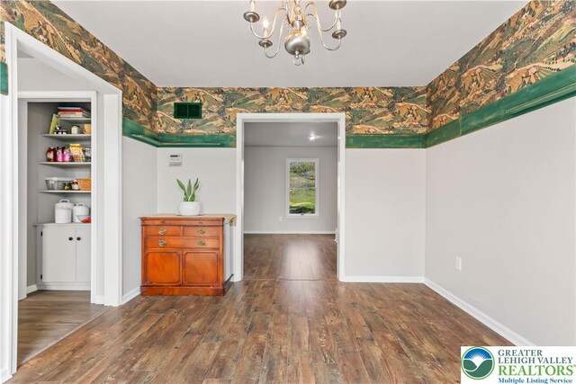 unfurnished dining area featuring baseboards, a notable chandelier, and hardwood / wood-style floors
