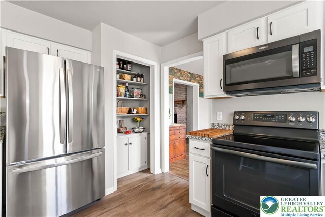 kitchen featuring freestanding refrigerator, black range with electric stovetop, white cabinetry, and wood finished floors
