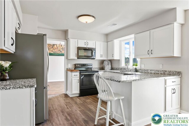 kitchen featuring white cabinets, stainless steel appliances, a peninsula, wood finished floors, and visible vents