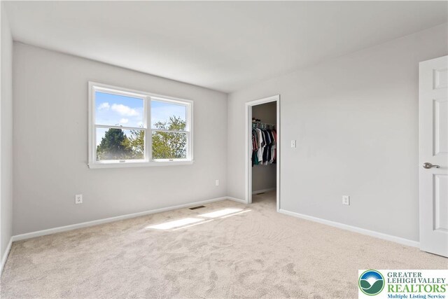 unfurnished bedroom featuring carpet floors, baseboards, visible vents, and a spacious closet