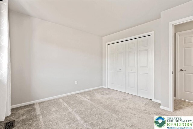unfurnished bedroom featuring carpet floors, baseboards, visible vents, and a closet
