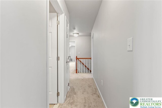 hallway featuring baseboards, light carpet, and an upstairs landing