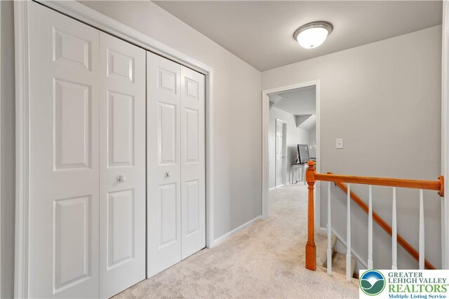 hall with baseboards, an upstairs landing, and light carpet