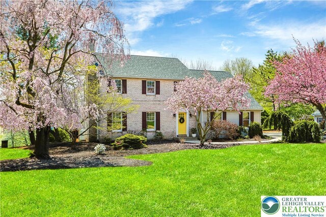colonial home featuring roof with shingles, a front lawn, and brick siding