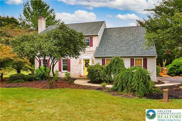 view of front of property featuring brick siding, a chimney, roof with shingles, and a front lawn