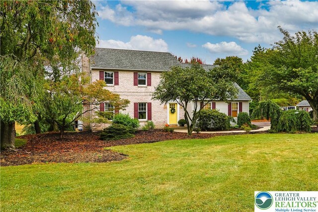 colonial home featuring brick siding, roof with shingles, and a front yard