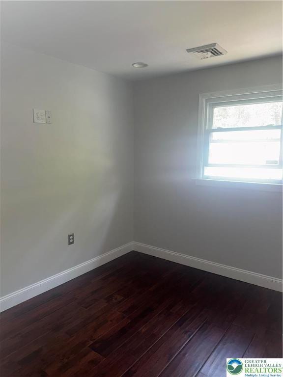 empty room featuring dark wood-style flooring, baseboards, and visible vents