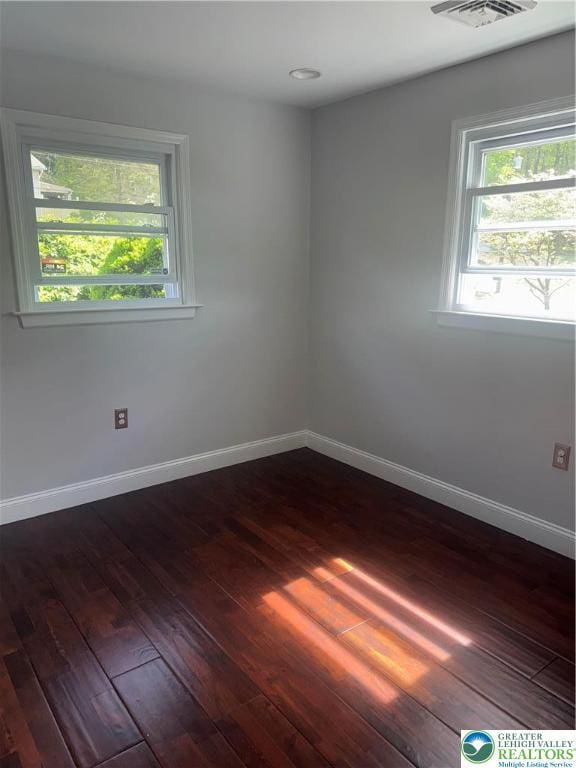 empty room with dark wood-type flooring, baseboards, and a wealth of natural light