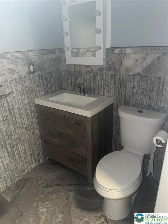 half bath featuring tile walls, vanity, and toilet