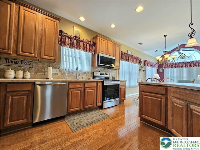 kitchen with an inviting chandelier, brown cabinets, a sink, appliances with stainless steel finishes, and backsplash