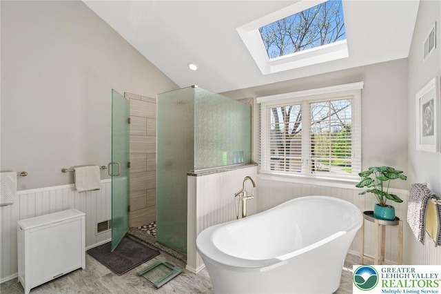 bathroom featuring wainscoting, vaulted ceiling with skylight, a freestanding tub, visible vents, and a stall shower