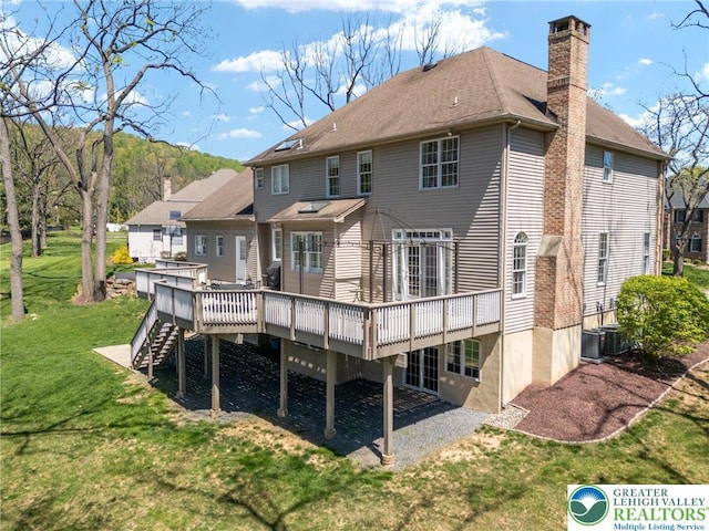 rear view of house with stairs, a deck, a chimney, cooling unit, and a lawn